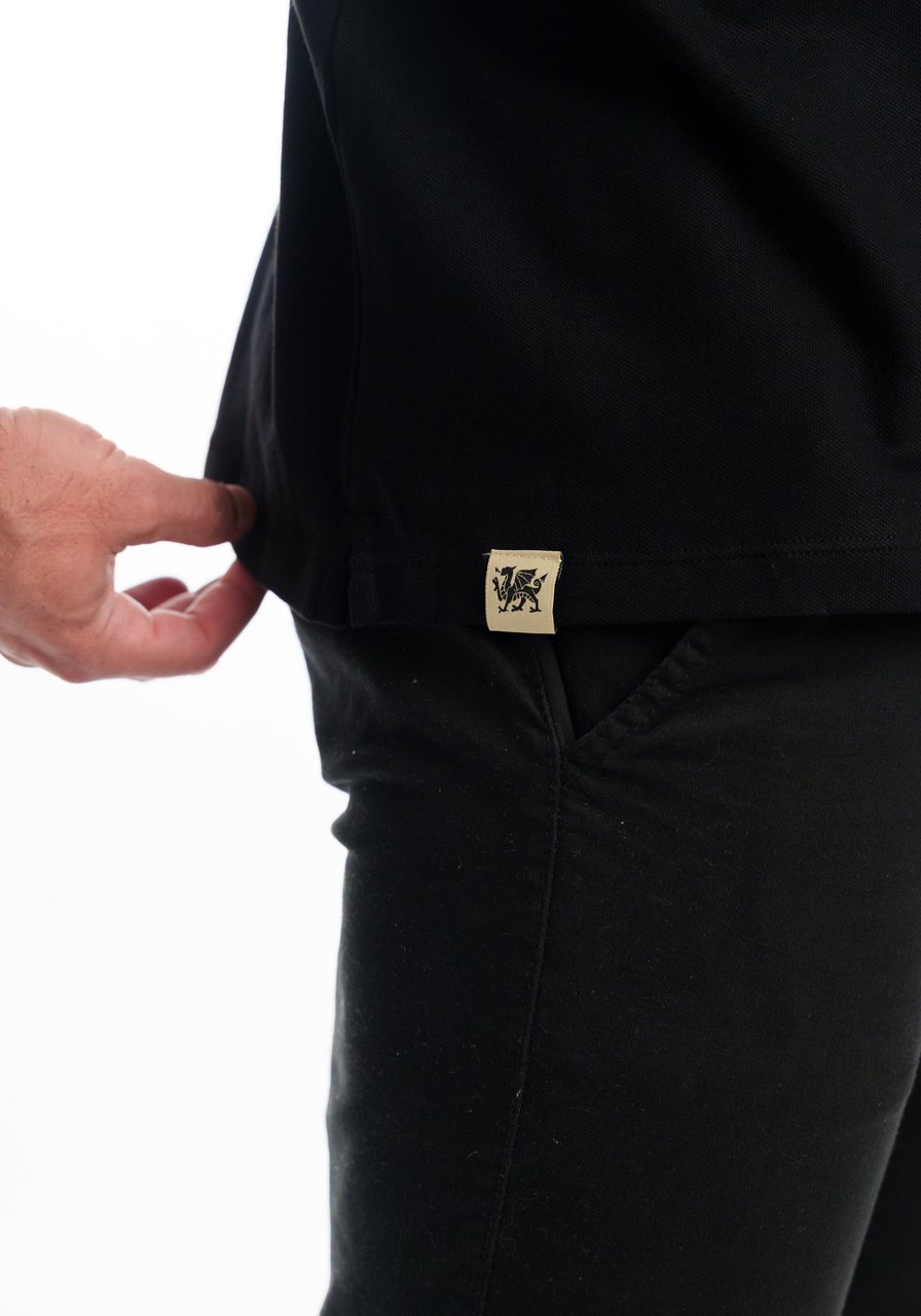 Detalhe do tecido Piquet Comfort e da etiqueta com o dragão na barra da polo preta Camboja Wear